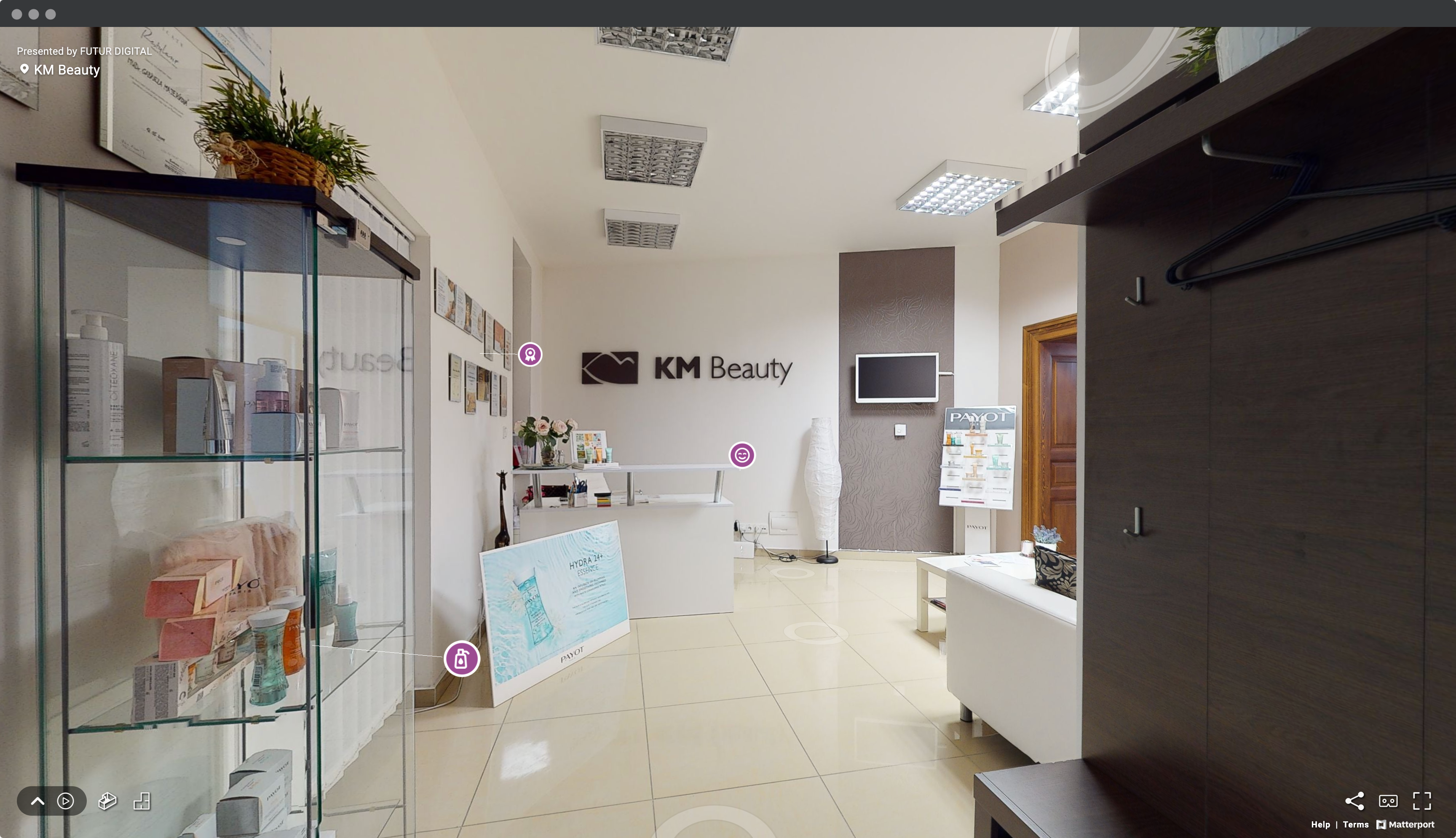 Screenshot okna prehliadača s virtuálnou prehliadkou kozmetického salóna KM Beauty so záberom na vstupnú halu s recepciou, sedačkou, stolom, virtínou s kozmetikou a označenými bodmi záujmu.