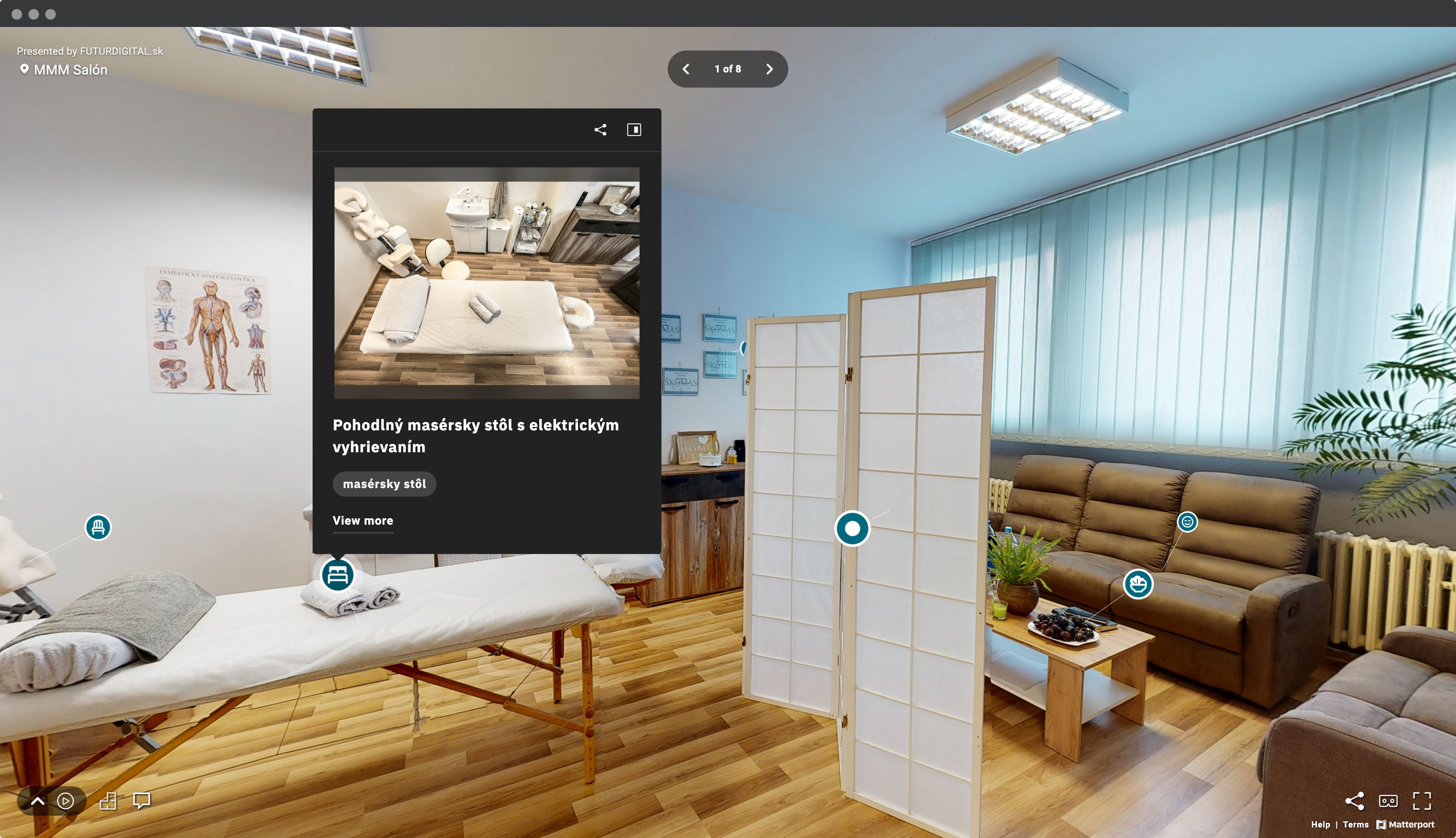 Screenshot okna prehliadača s pohľadom na virtuálnu prehliadku masážneho salóna MMM Salón so záberom priestor s masážnym stolom, masážnou stoličkou, paravánom, sedacou súpravou a označeným bodom záujmu - fotografia masážneho stola s popisom vybavenia.