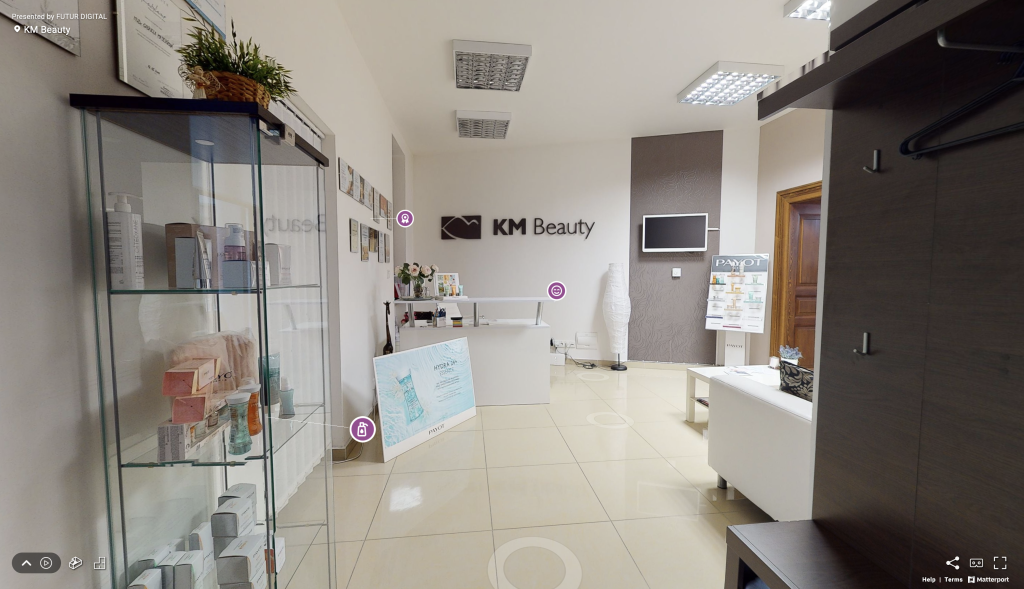 Pohľad na virtuálnu prehliadku kozmetického salóna KM Beauty s pohľadom na vstupnú halu s recepciou, vitrínou s produktami značky Payot a sedacou súpravou.