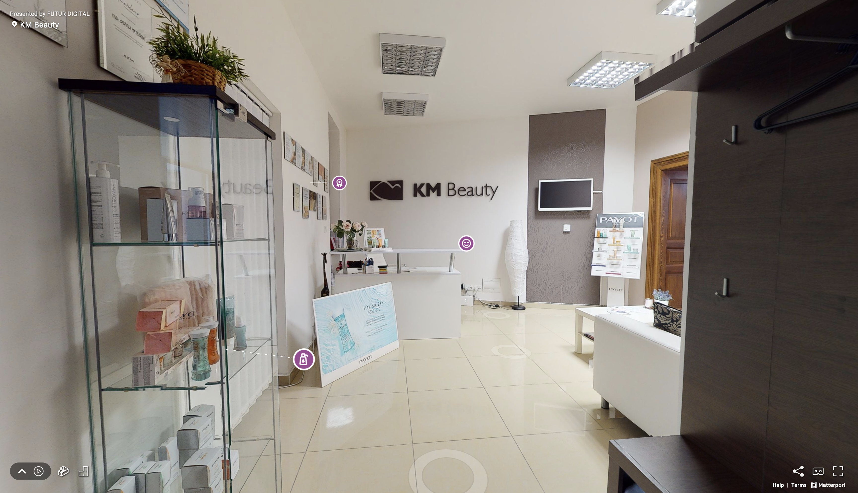 Pohľad na virtuálnu prehliadku kozmetického salóna KM Beauty s pohľadom na vstupnú halu s recepciou, vitrínou s produktami značky Payot a sedacou súpravou.