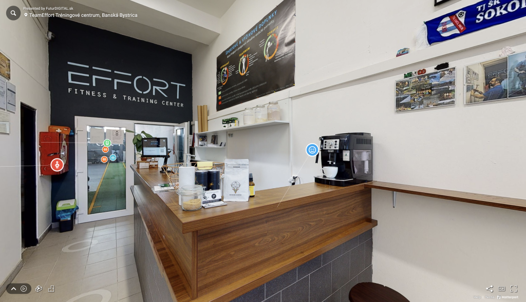 Pohľad na virtuálnu prehliadku fitnesscentra Team Effort s pohľadom na vstupnú halu s barovým pultom, kávovarom, stenou s certifikátmi a ponukou doplnov výživy.